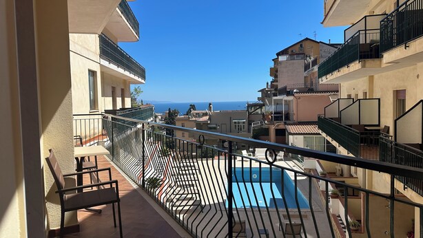 A balcony with a pool, outdoor furniture, and a view of the sea. - Hotel Soleado (Taormina)