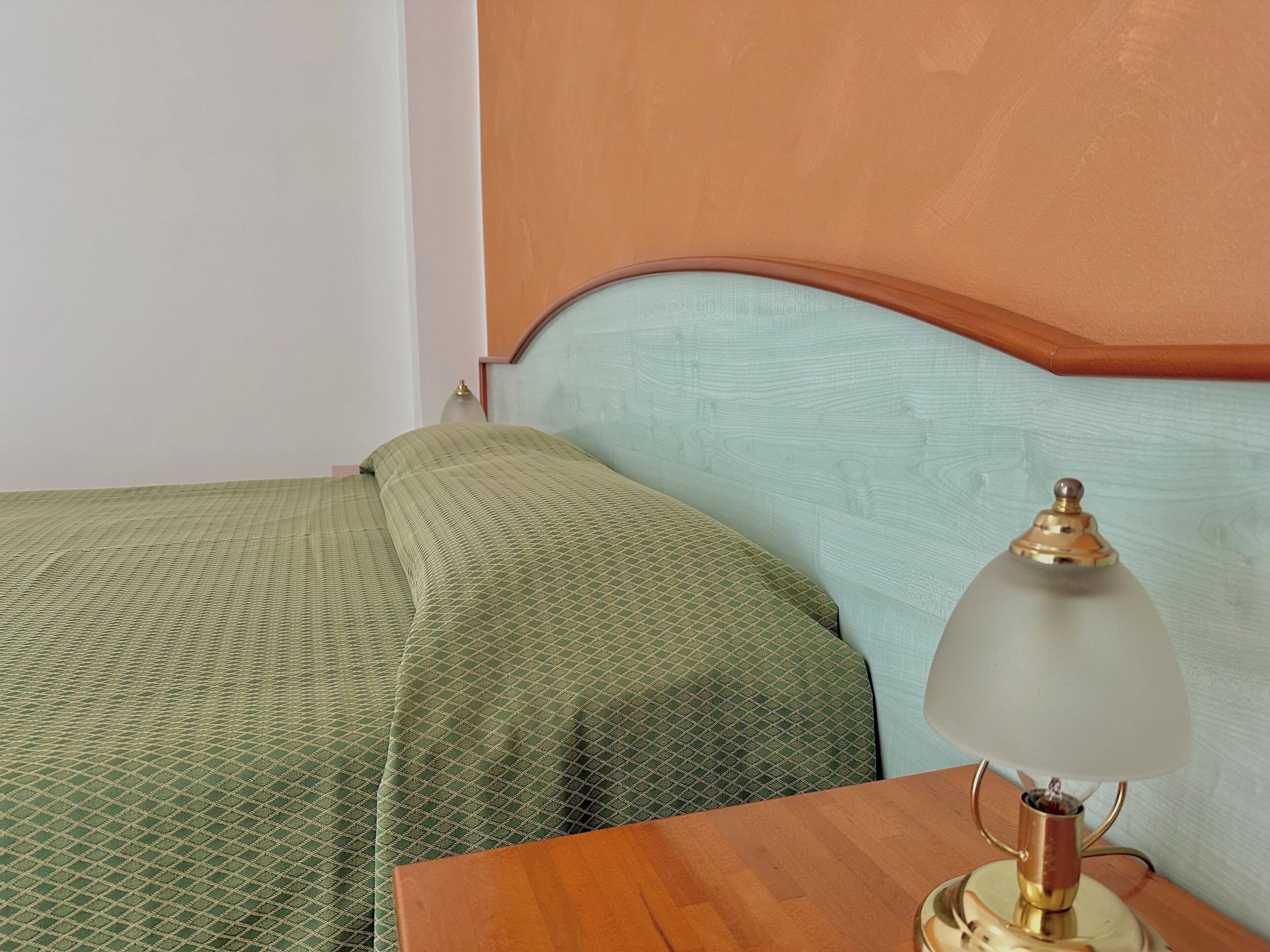 A bed with green bedding, a wooden nightstand, and a lamp with a white shade.