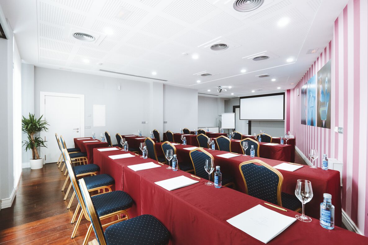 Ein Konferenzraum mit langen Tischen, Stühlen und einer Projektionsleinwand.