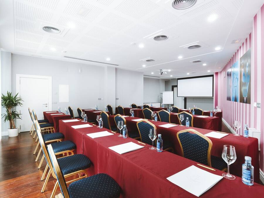 Ein Konferenzraum mit langen Tischen, Stühlen und einer Projektionsleinwand.