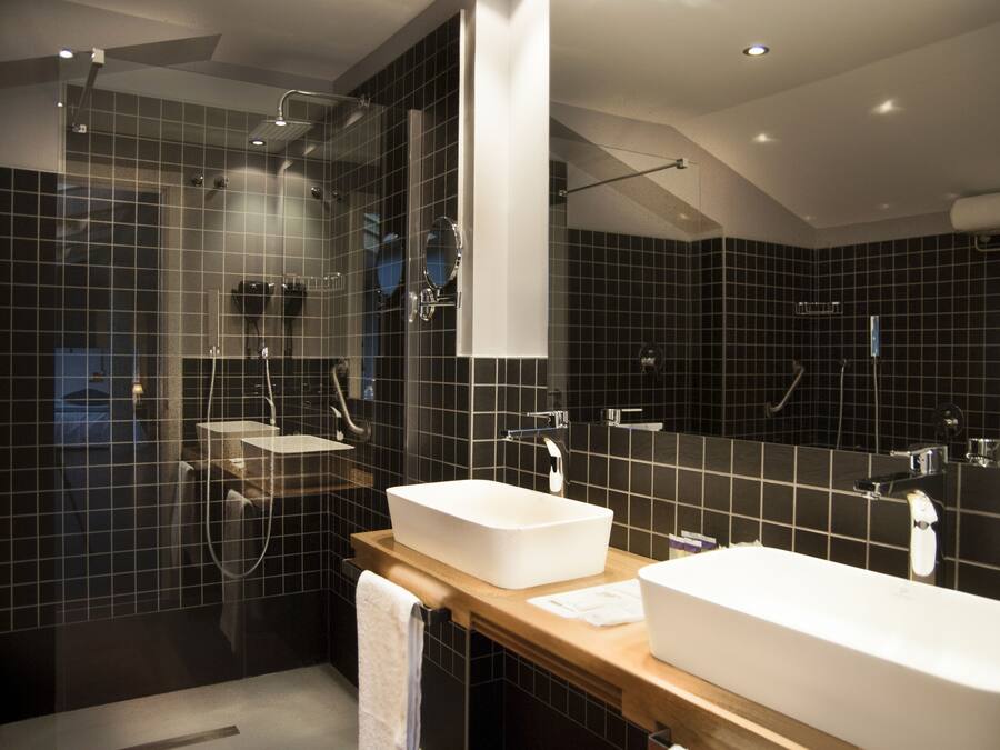 A modern bathroom with two sinks, a shower, and a large mirror.
