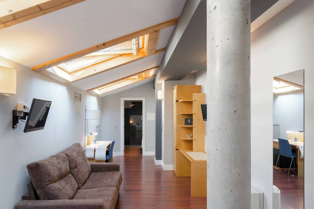 A modern loft with wooden beams, a concrete pillar, a sofa, and a desk area.