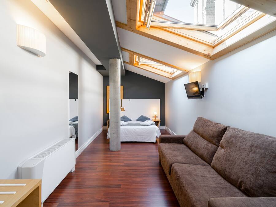 Un dormitorio moderno y luminoso con tragaluces, una cama grande, un sofá marrón y un televisor de pantalla plana.