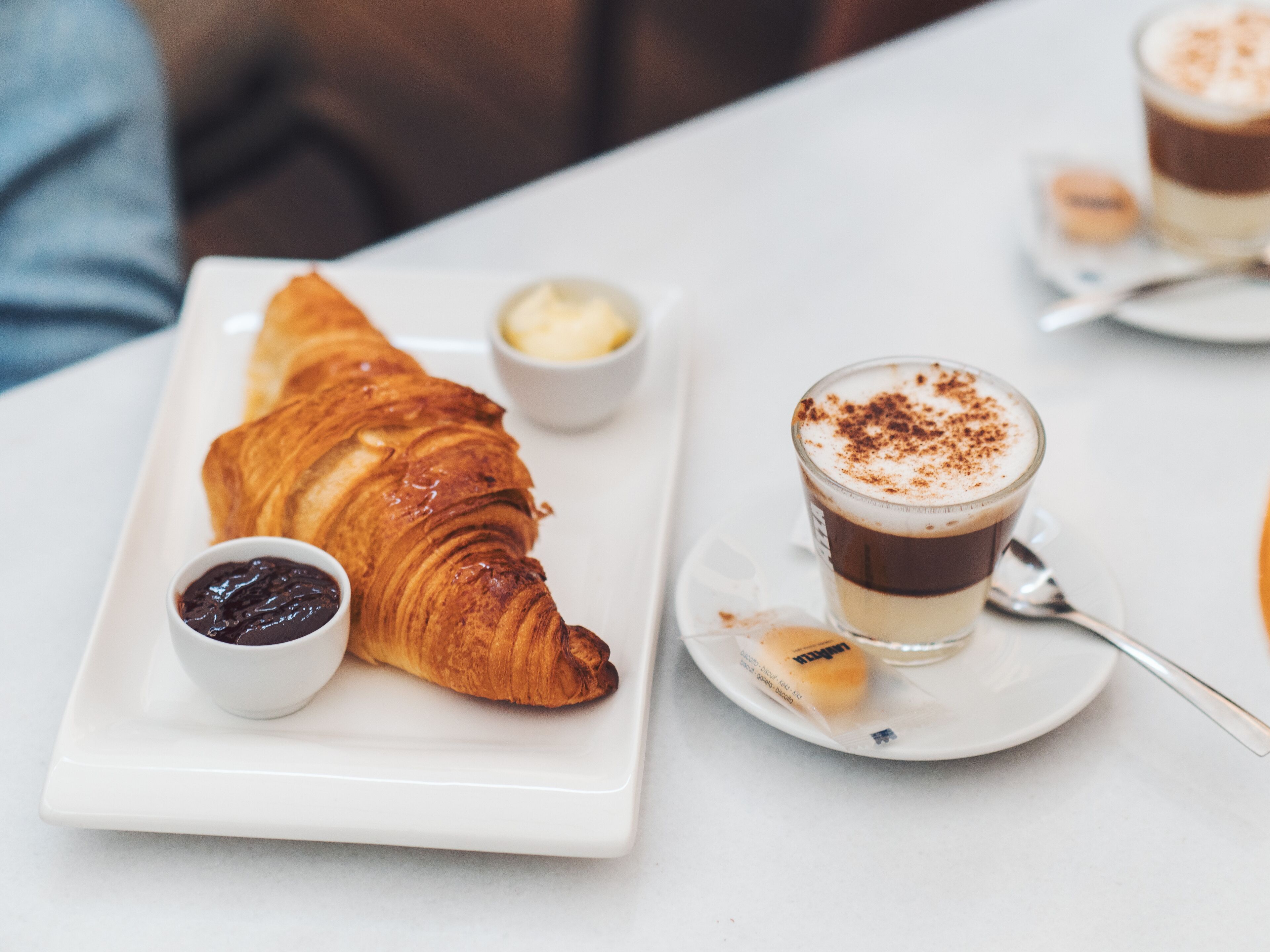 A croissant with a small bowl of jam and a cup of coffee on a white plate.
