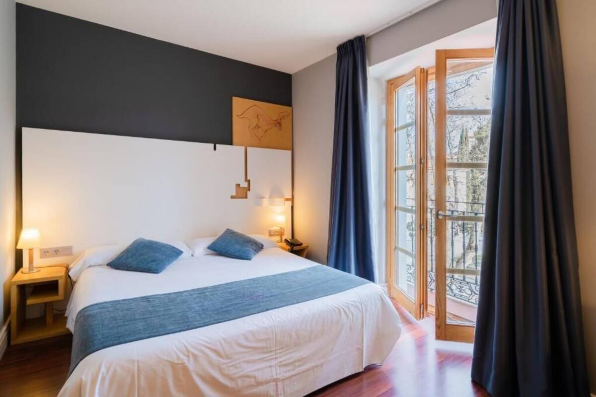 A hotel room with a large bed, bedside lamps, a view of the outdoors, and a window with curtains.