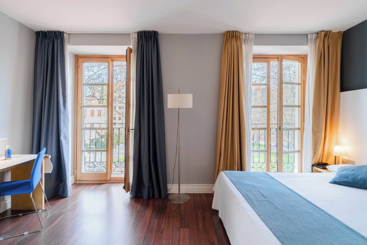 A hotel room with a bed, desk, chair, and a floor lamp.
