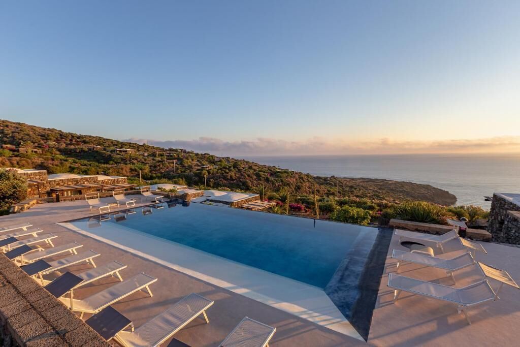 Ein Poolbereich mit Liegestühlen und Blick auf das Meer.