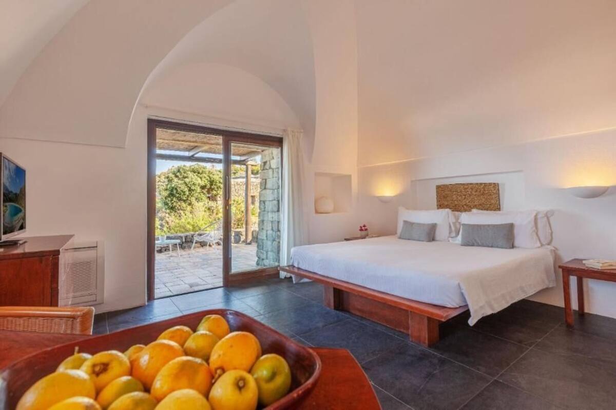 A bedroom with a large bed, a wooden nightstand, a TV, and a fruit bowl on a table.