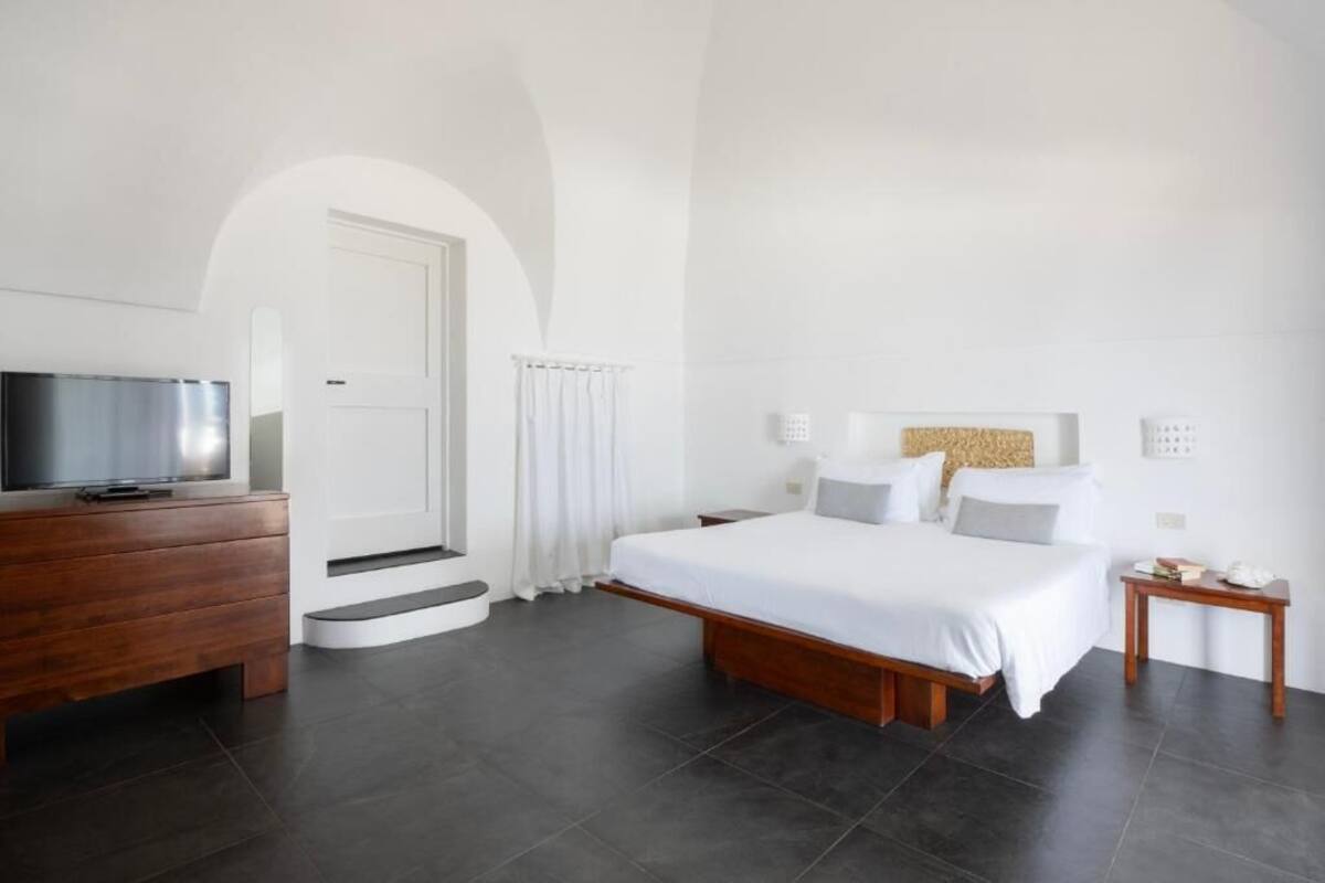 A modern hotel room with a large bed, a wooden dresser, a TV, and a staircase leading to another room.