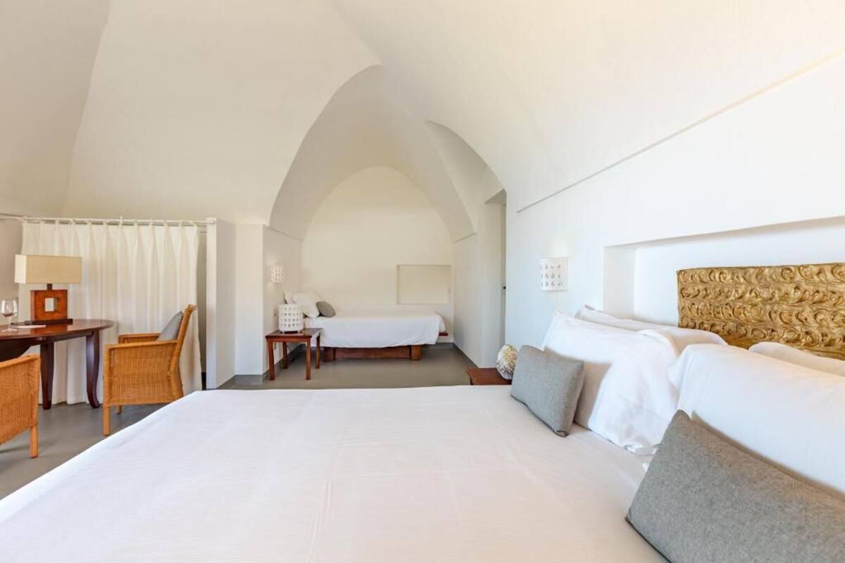 A hotel room with a large bed, a desk with a chair, a small table, and a sofa.