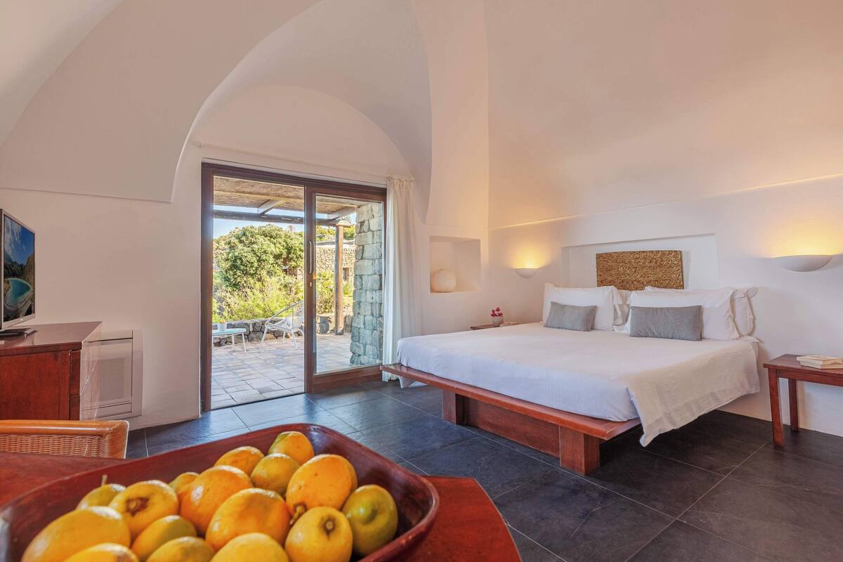 Une chambre à coucher avec un lit, une table de chevet, une télévision, un panier de fruits et une vue sur l’extérieur.