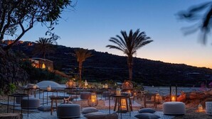 An outdoor seating area with tables, chairs, and lanterns, set against a hillside backdrop.