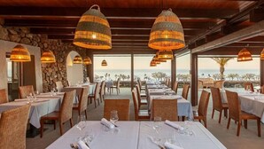 A restaurant with tables set for dining, large hanging lamps, and a view of the ocean.