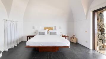 A bedroom with a large bed, a stone wall, and a view of the outside.