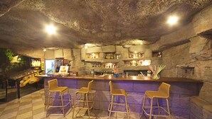 An indoor bar with a stone wall backdrop, bar stools, and a variety of bottles and glasses on shelves. - Hotel Selen (Marmaris)