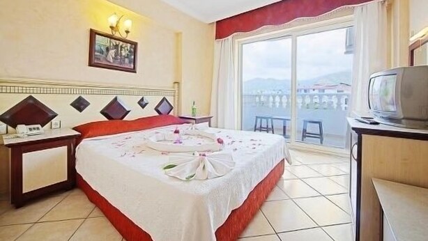 A hotel room with a bed, a bedside table, a TV, and a large window with a view. - Hotel Selen (Marmaris)