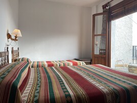 Habitación con dos camas, cabecera de madera, lámpara de pared y un amplio ventanal con vista a un edificio.