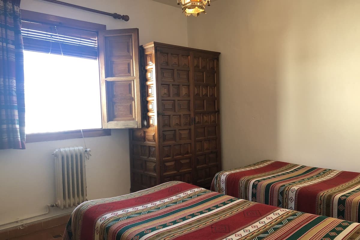 A room with two beds, a radiator, a window with curtains, and a wooden wardrobe.
