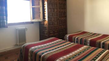 Una habitación con dos camas, un radiador, una ventana con cortinas y un armario de madera.