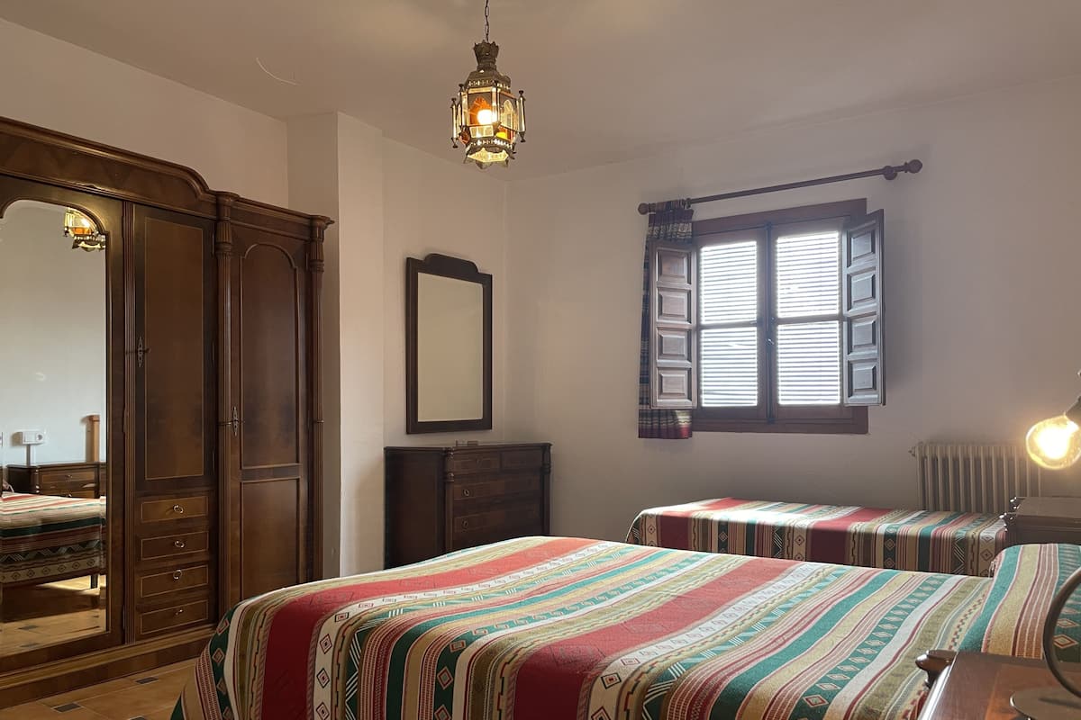 A room with two beds, a wooden wardrobe, a mirror, and a window with shutters.