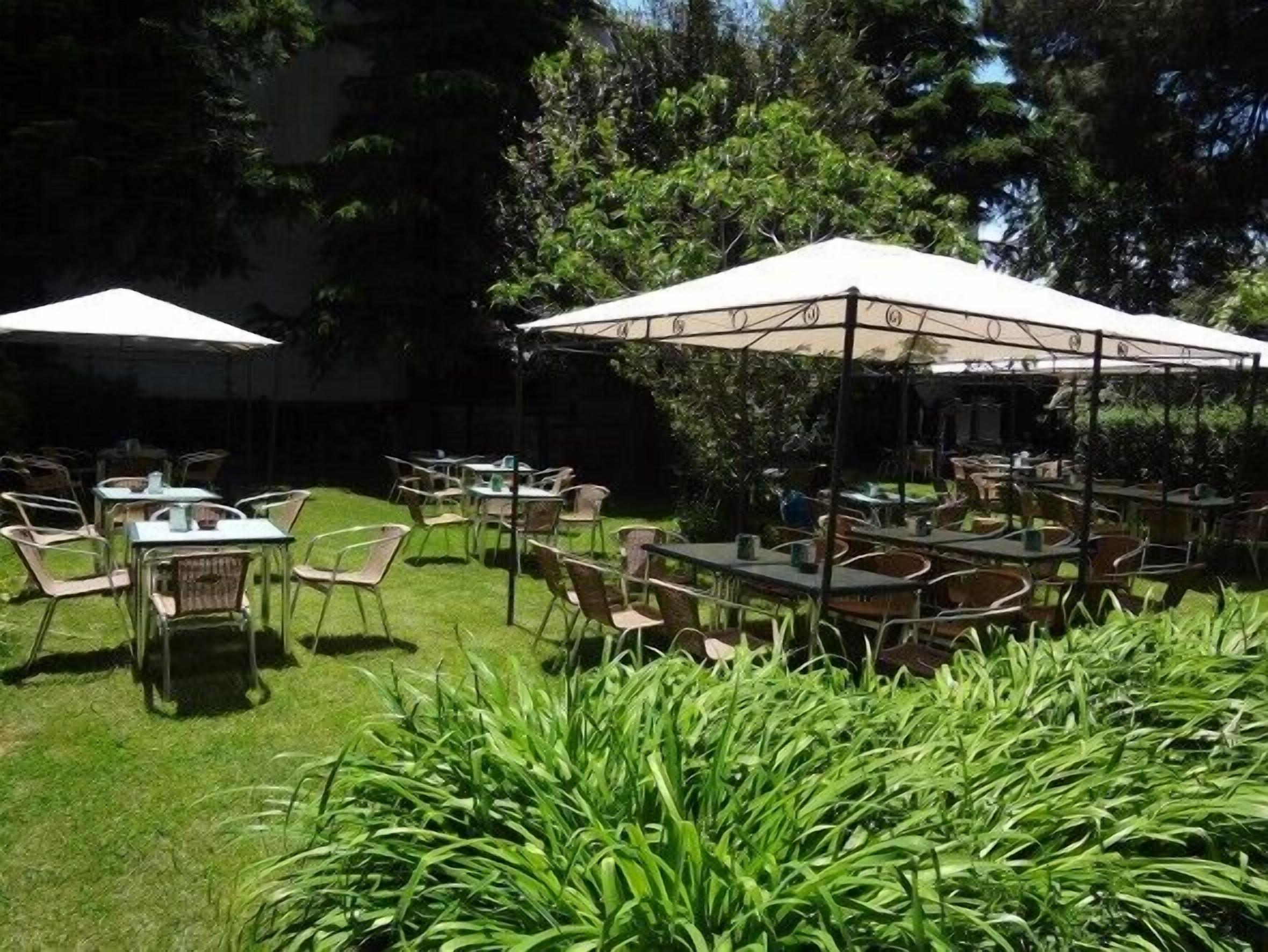 An outdoor patio with tables and chairs under white umbrellas, surrounded by lush greenery.