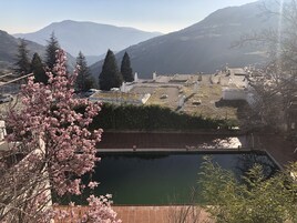 Vista de un cementerio con lápidas y un estanque, rodeado de montañas y árboles.