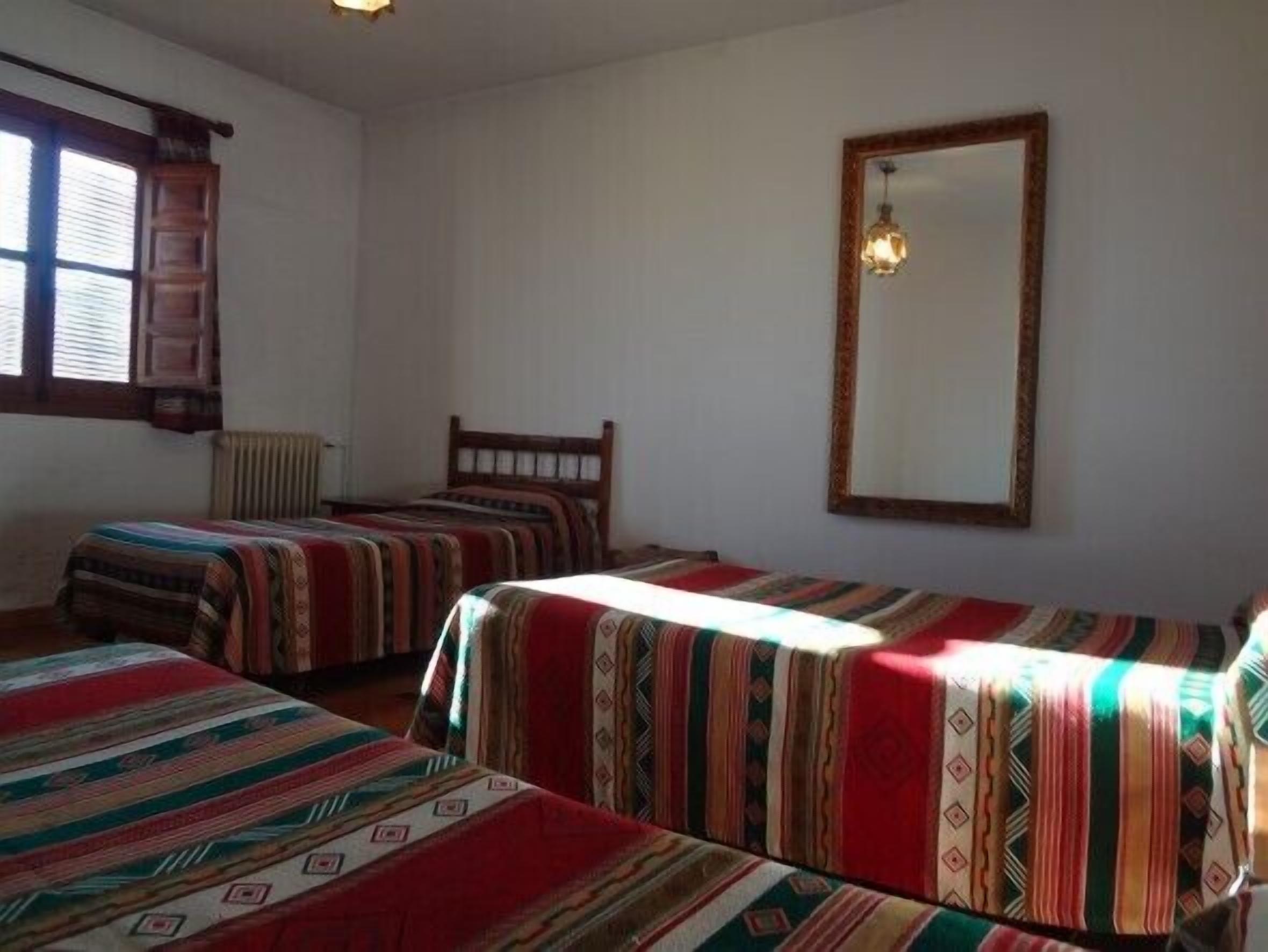 Et værelse med to senge, en træsenggavl, en radiator, et vindue med rullegardiner og en hængende lampe.