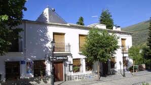 A two-story building with a white facade, a tiled roof, and a balcony with metal railings. - Hostal Poqueira (Capileira)