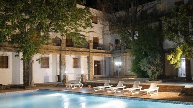 A pool area with lounge chairs and a building with balconies. - Hostal Poqueira (Capileira)