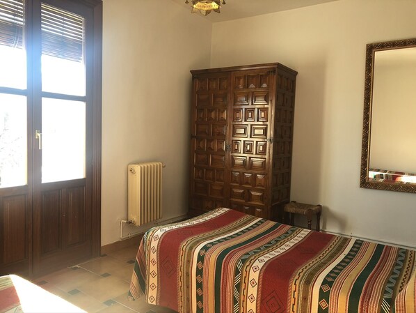 Une pièce comprenant une armoire en bois, un radiateur, un lit recouvert d’une couvre-lit à motifs et un miroir accroché au mur.