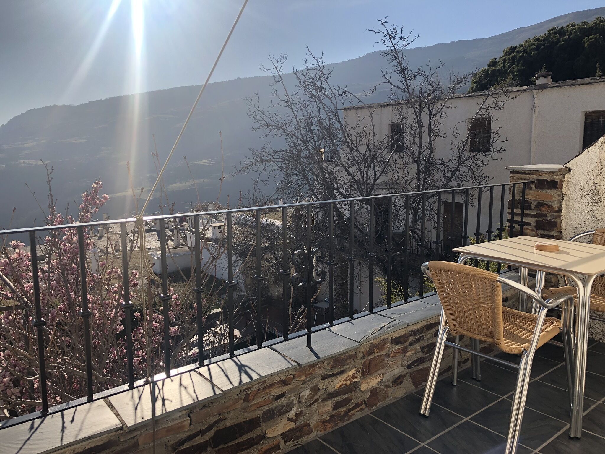 Un balcon avec un mur en pierre, une rambarde en métal et une table avec des chaises.