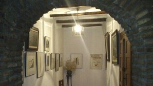 A narrow hallway with a wooden bench, framed pictures on the walls, and a small table with a vase. - Hostal Poqueira (Capileira)