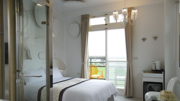 Habitación de hotel con cama, escritorio, silla, balcón y vistas al exterior.