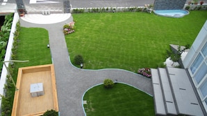 Un césped bien cuidado con una terraza de madera, una piscina y un camino pavimentado.