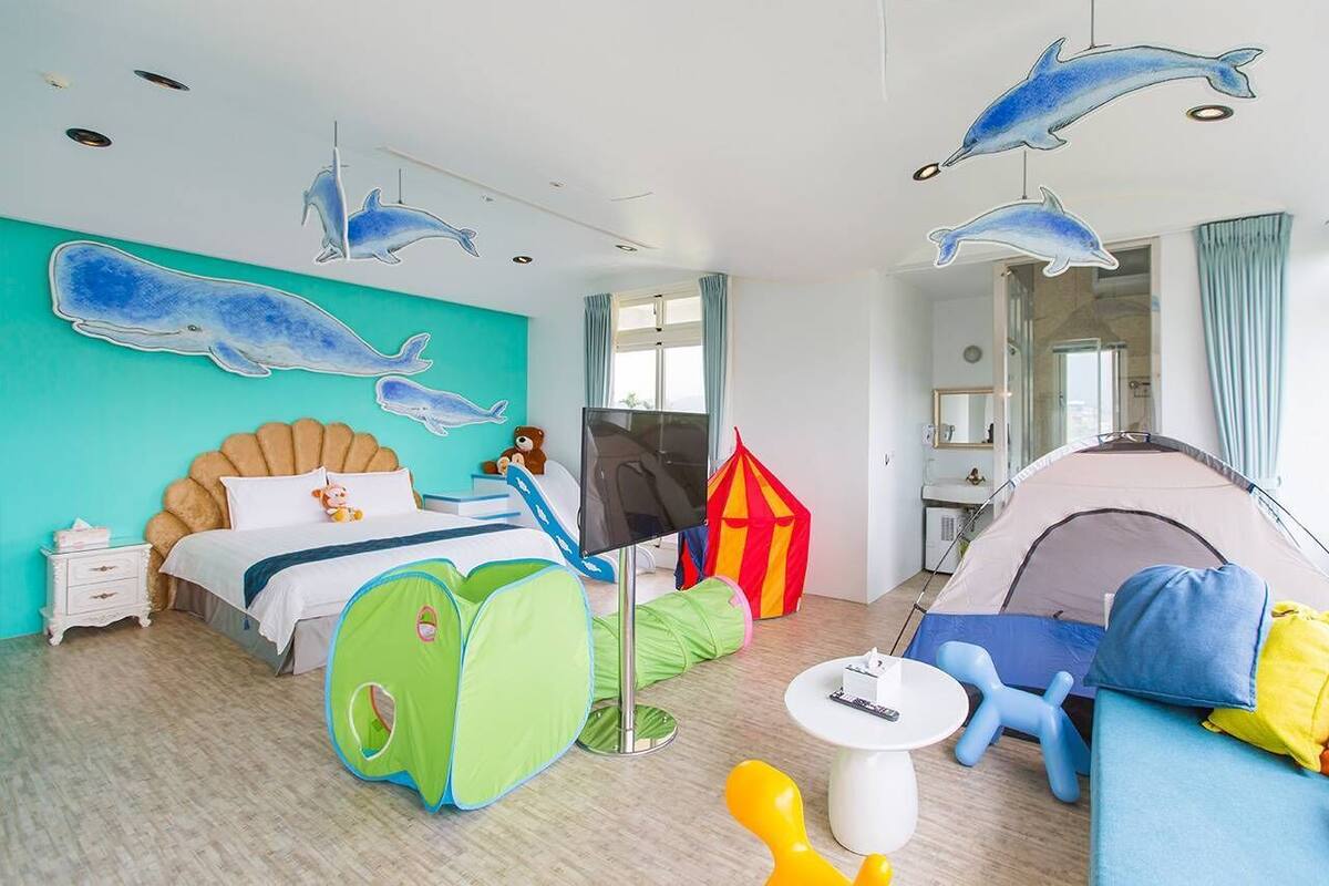 A child-friendly room with a bed, a tent, a play tent, a sofa, and a television.