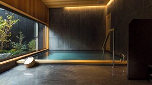 A modern spa room with a large window, a wooden bench, and a stone floor. - Shinpuro (Miyazu)