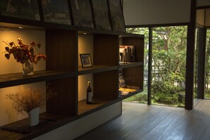 Un interior moderno con suelo de madera, una estantería con diversos objetos y vistas a zonas verdes.