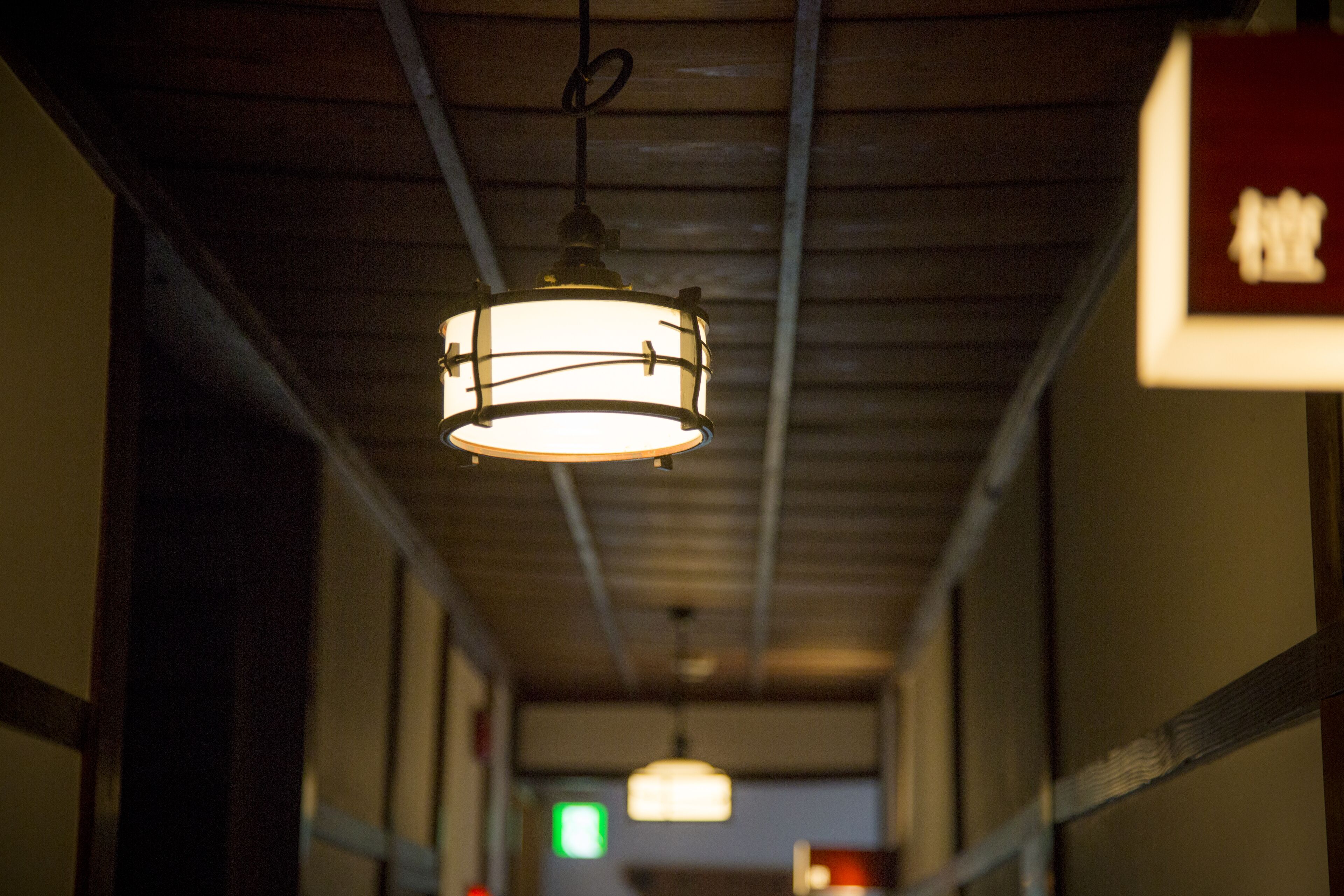 A corridor with hanging pendant lights and a visible exit sign.