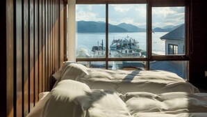 A bedroom with a large window overlooking a body of water and a docked boat. - Shinpuro (Miyazu)