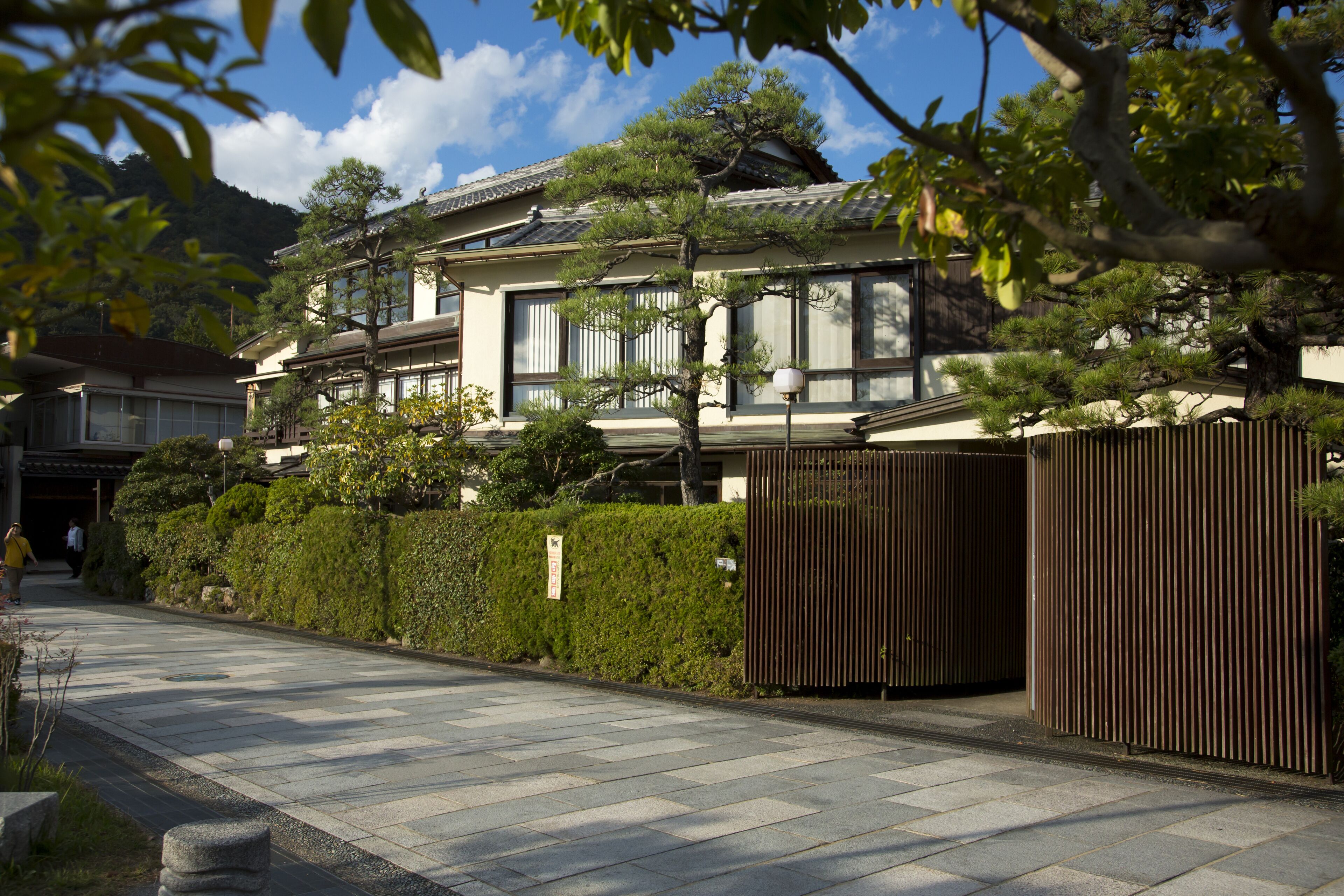 Una casa tradicional japonesa con techo de tejas, ventanas amplias y un jardín bien cuidado con valla de madera.