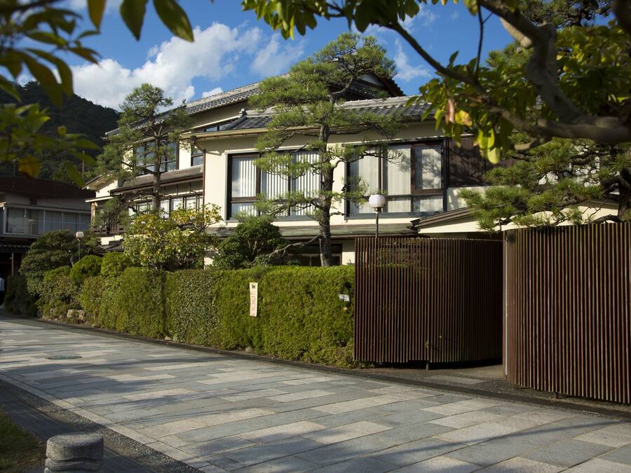 Una casa tradicional japonesa con techo de tejas, ventanas amplias y un jardín bien cuidado con valla de madera.