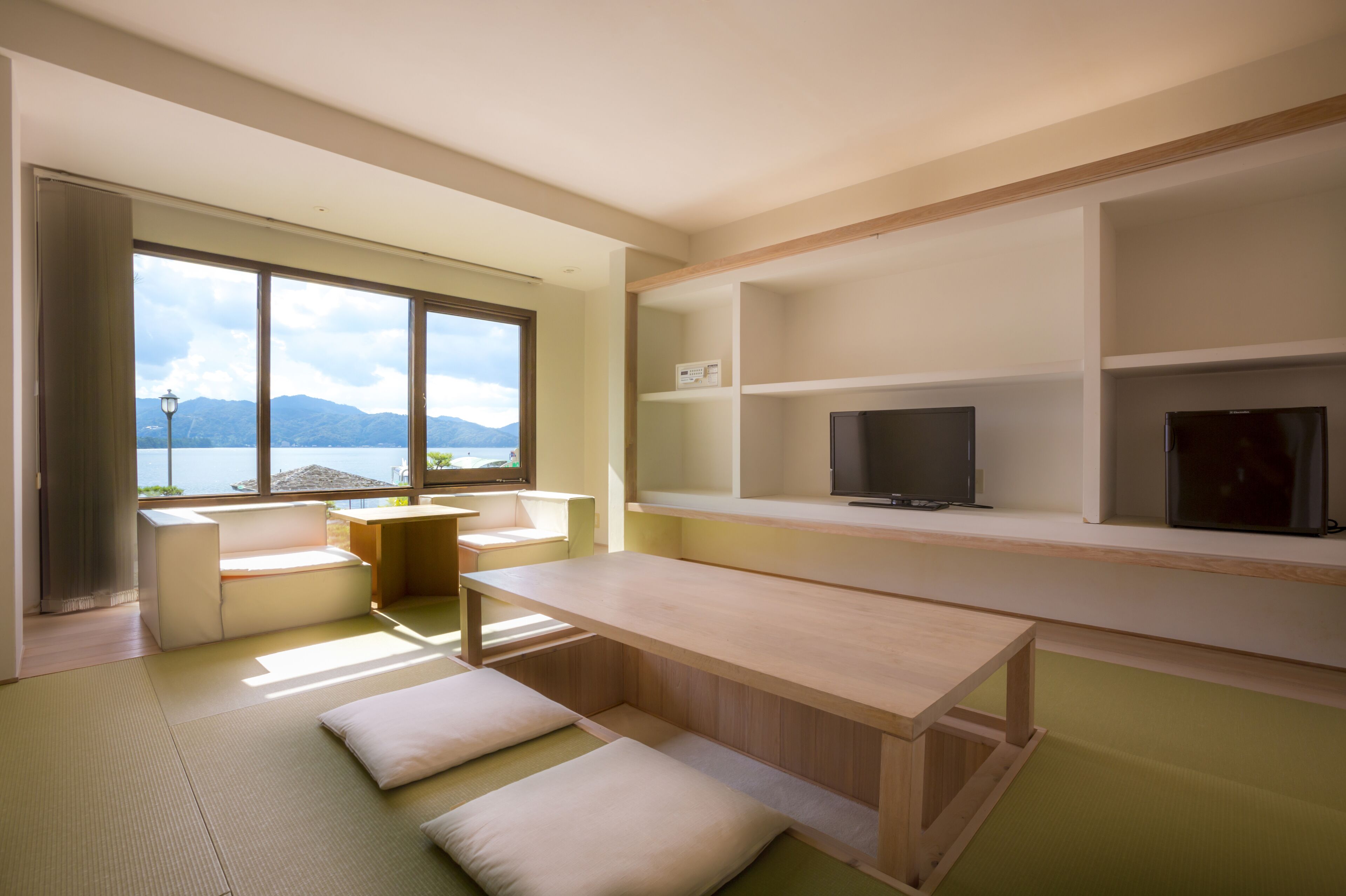 Ein modernes Zimmer mit Tatami-Böden, einem niedrigen Holztisch, einer Couch und einem Fernseher auf einem Regal.