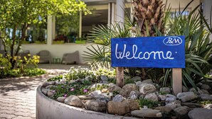 Une pancarte d’accueil ornée du logo « R&M », placée dans un espace paysager agrémenté de rochers et de plantes.