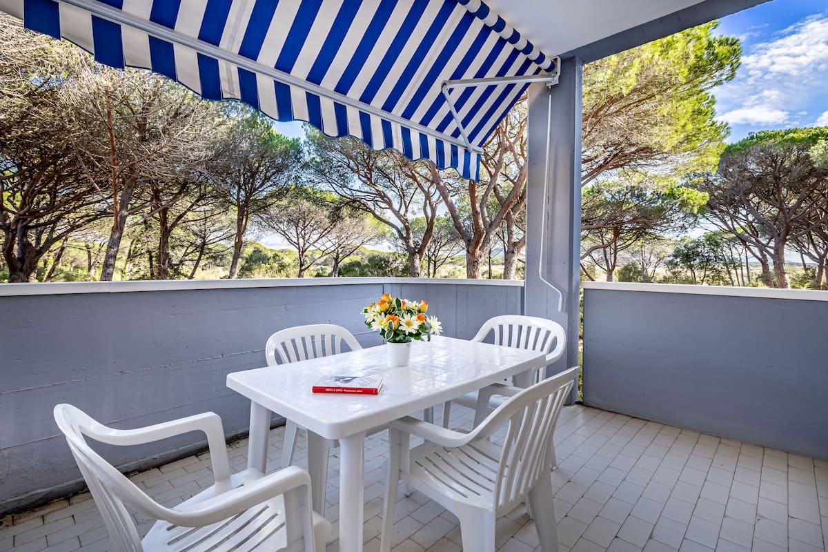 A covered outdoor seating area with a table and chairs, a potted plant, and a book on the table.