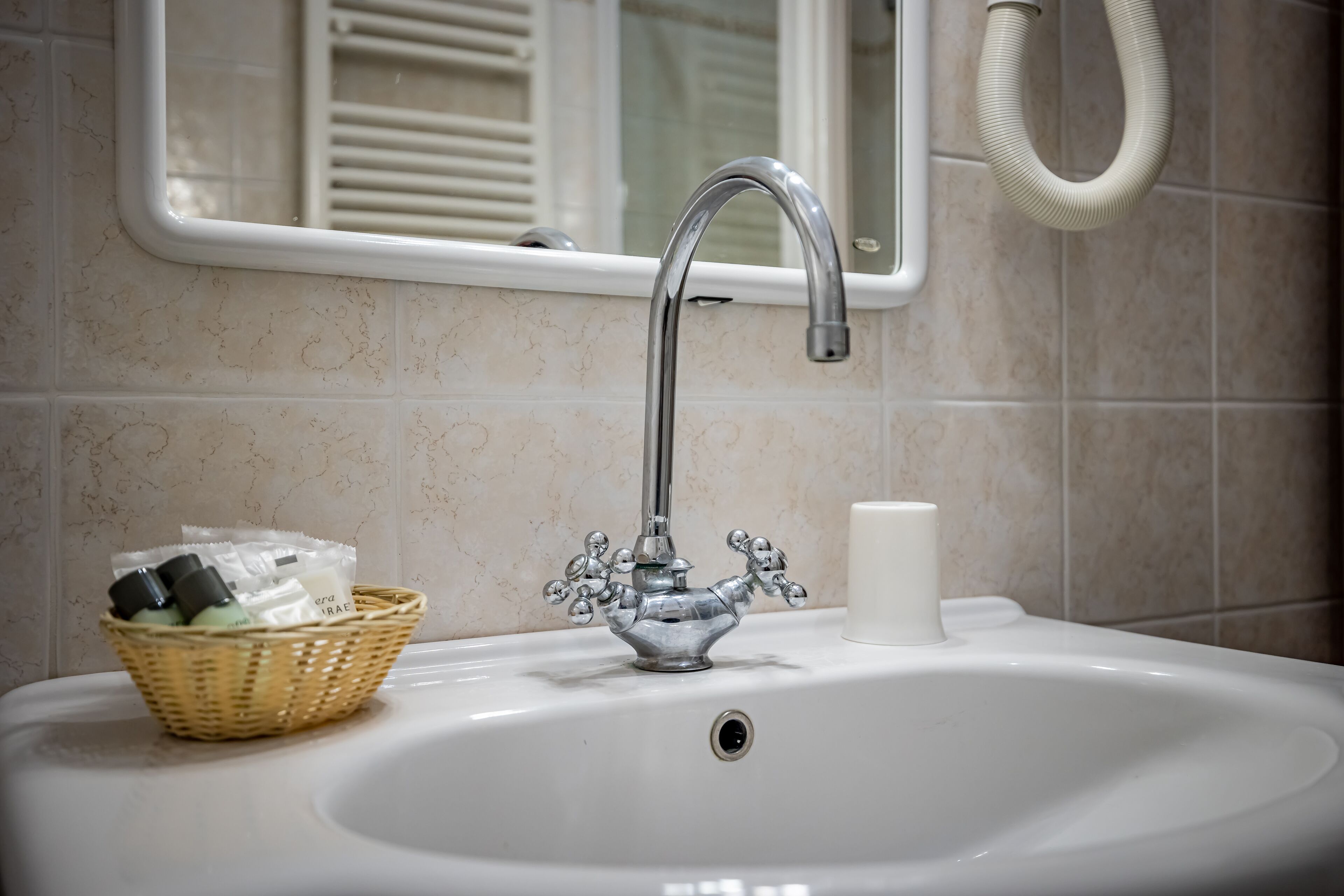 Een badkamermeubel met een chromen kraan, een witte zeepdispenser en een rieten mand met toiletartikelen.
