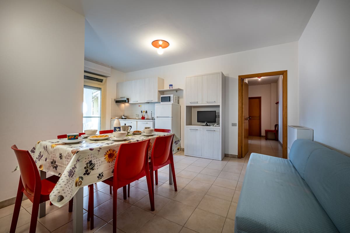 A compact kitchen with white cabinets, a dining table with red chairs, and a blue sofa.