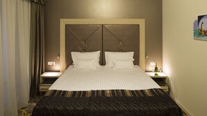 Una habitación de hotel con una cama grande, dos mesitas de noche, un paralelo, una lámpara de pared y un cuadro.