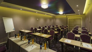 Un salón de conferencias con filas de mesas, sillas y una pizarra.