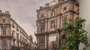 Una habitación con sillas amarillas, una mesita pequeña, una planta en maceta y un mural con edificios.