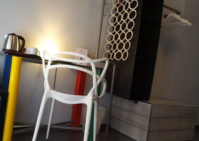 A white chair with a unique circular backrest design, a yellow and blue cabinet, and a red and white striped object.